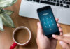 Typing privacy passcode on smartphone near laptop and coffee.