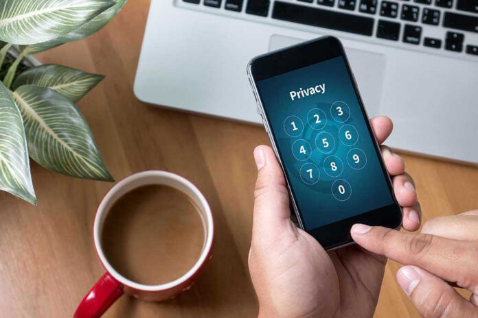 Typing privacy passcode on smartphone near laptop and coffee.