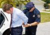 A police officer handcuffing a man in formal attire outside a police car