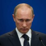 Oil Shock Bonanza—Russia Cashes In Big Time A serious-looking man in a suit at a press conference with a blue background