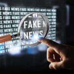 Poll Shocker: Media Rhetoric or Shooter to Blame? A hand pointing at the words 'FAKE NEWS' magnified by a glass