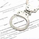 Teen Found In Dryer After 911 Call Handcuffs on top of an arrest warrant document.