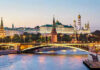 Illuminated bridge and Kremlin complex across river at twilight.