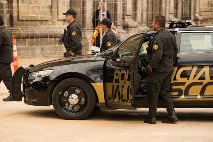 Police officers standing and sitting near a patrol car.