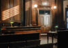 Former National Security Adviser’s Plea Raises Double-Standard Alarms Empty courtroom with wooden interior and green lamps.