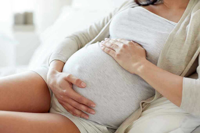 564114571 Pregnant woman holding her belly, sitting comfortably.