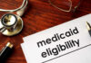 Ghost Rides Bilk Medicaid — Kickbacks Exposed Stethoscope pen document about Medicaid eligibility on table