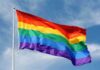 A rainbow flag waving against a blue sky
