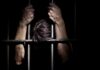 Hands gripping prison bars in a dark setting