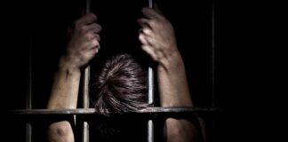 Hands gripping prison bars in a dark setting