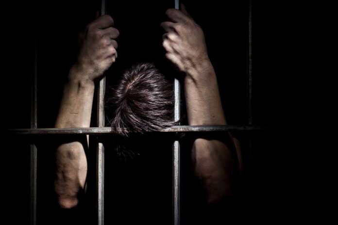 Hands,Of,The,Prisoner,On,A,Steel,Lattice,Close,Up Hands gripping prison bars in a dark setting