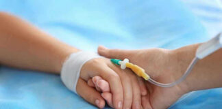 Two hands holding, one with medical IV attached.