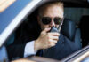 Intel War Erupts Inside Langley Man in suit using walkie-talkie in car.