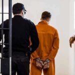 Prisoner in orange jumpsuit handcuffed and escorted by officer