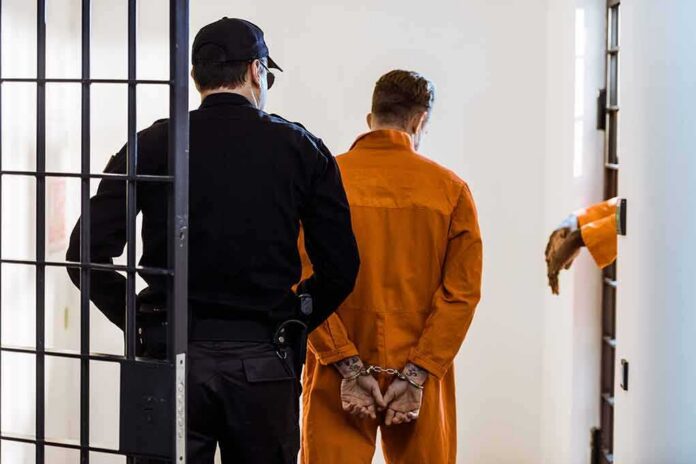 Prisoner in orange jumpsuit handcuffed and escorted by officer