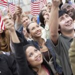 A diverse group of people joyfully waving American flags in celebration