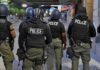 Police officers in riot gear stand on a city sidewalk at night