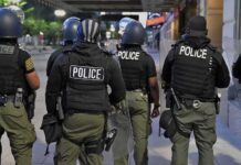 Police officers in riot gear stand on a city sidewalk at night
