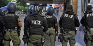 Police officers in riot gear stand on a city sidewalk at night