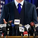 A speaker at a press conference with multiple microphones in front of them