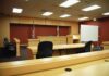 Judge Drops Bombshell On Singer Interior view of an empty courtroom with wooden furniture and American flags