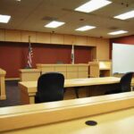 Judge Drops Bombshell On Singer Interior view of an empty courtroom with wooden furniture and American flags