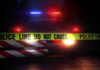 Police car behind crime scene tape at night