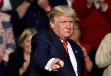 Trump’s Chilling Line Stuns Crowd man in suit pointing toward the camera at an event