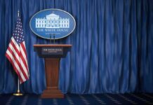 White House press briefing podium with U.S. flag and blue curtain