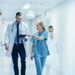 Doctor Ousted—Abortion Ultimatum Exposed Doctors walking in a hospital corridor reviewing a tablet