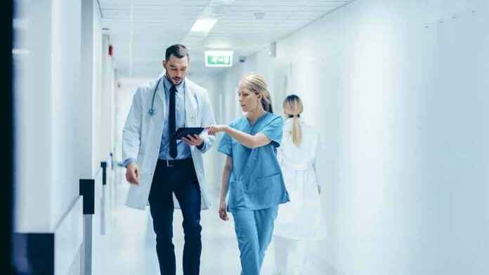 shutterstock_1189798168 Doctors walking in a hospital corridor reviewing a tablet