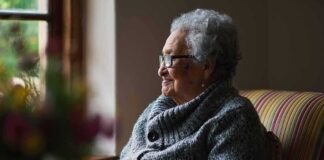 Elderly woman sitting by a window in a cozy sweater