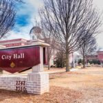 City Manager Benched—Gets a Raise City Hall sign in front of a red-brick municipal building