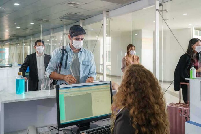 shutterstock_1873683787 masked travelers line up at an airport check-in counter