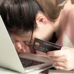 woman resting head on laptop while holding a credit card