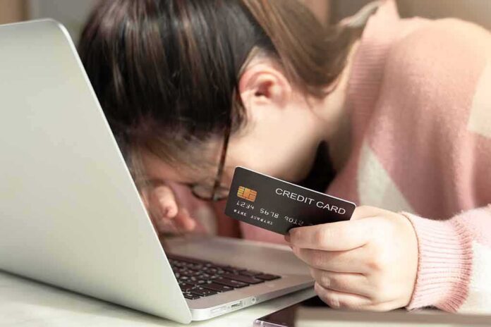 shutterstock_1887982108 woman resting head on laptop while holding a credit card