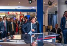 News anchor at a studio desk with crowd and cameras in background