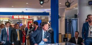 News anchor at a studio desk with crowd and cameras in background