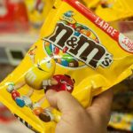 Hand holding a large yellow bag of M&M's peanut candy