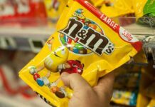Hand holding a large yellow bag of M&M's peanut candy