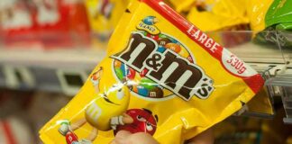 Hand holding a large yellow bag of M&M's peanut candy