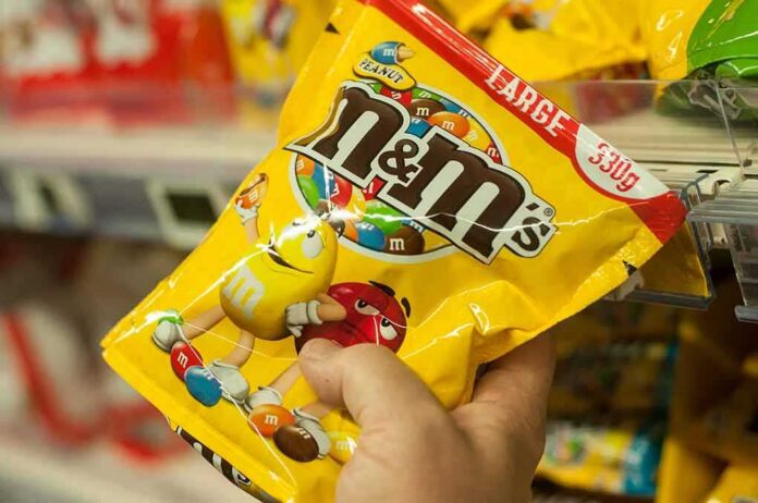 shutterstock_1031044987 Hand holding a large yellow bag of M&M's peanut candy
