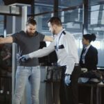 Airport security officer scanning a passenger with a handheld metal detector