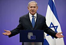 Arrest Standoff Explodes Before UN Week man in suit speaking at a podium with Israeli flag