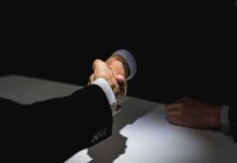 Two people in suits shaking hands over a table