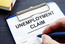 Unemployment claim form on clipboard with hand holding pen