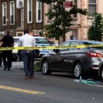 Police at urban street crime scene with yellow tape around parked cars