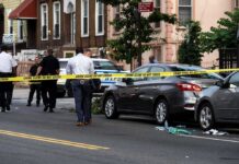 Police at urban street crime scene with yellow tape around parked cars
