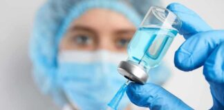Healthcare worker drawing blue liquid from vial with syringe