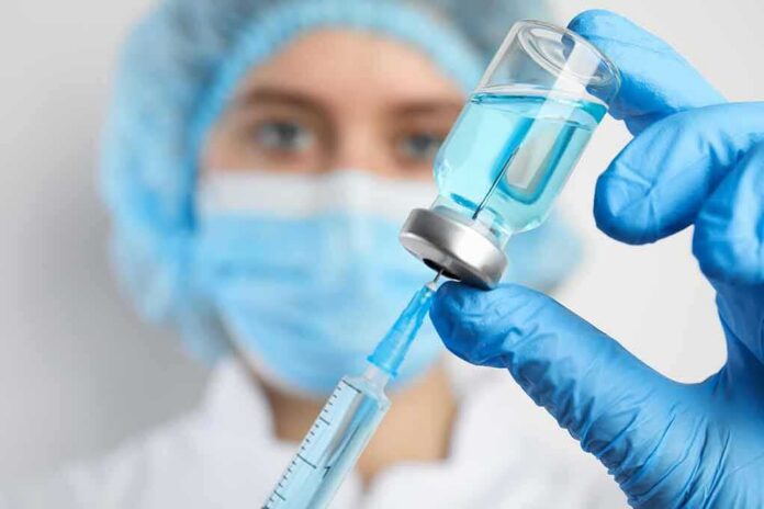 shutterstock_1730302936 Healthcare worker drawing blue liquid from vial with syringe